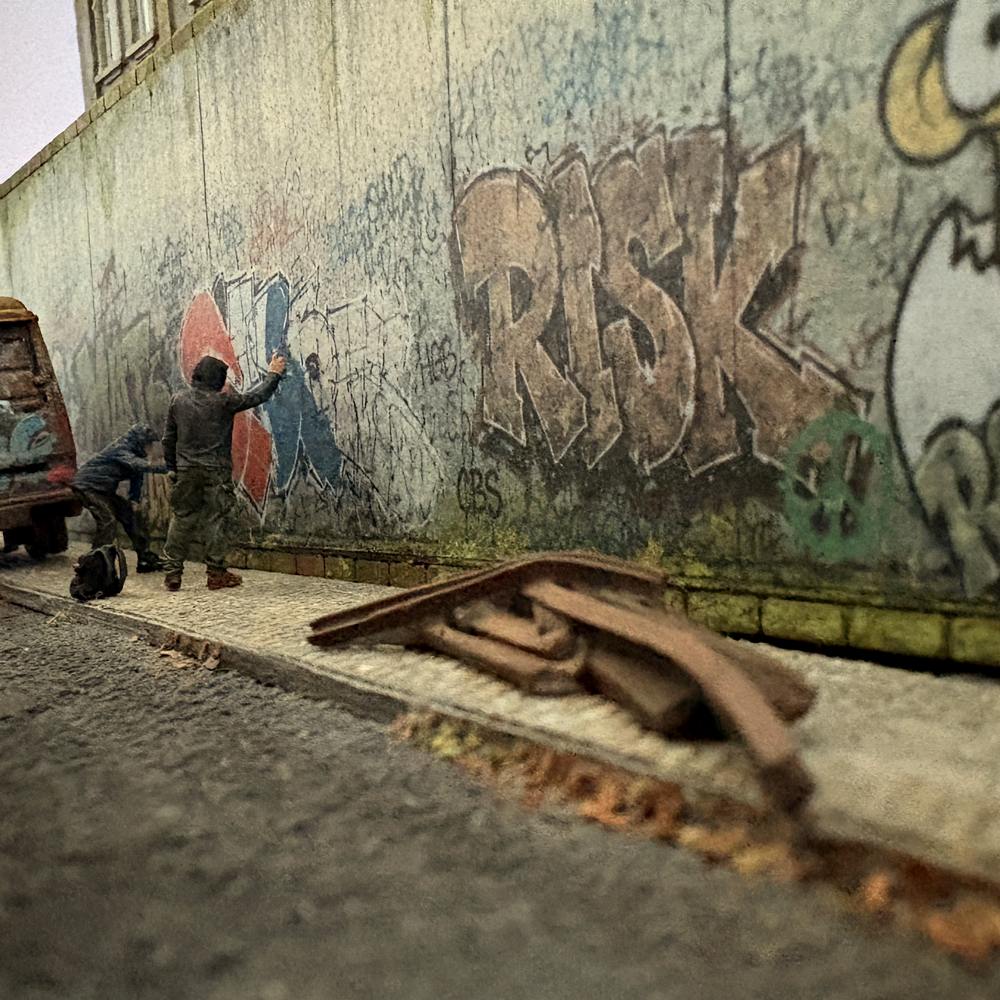 H0-Diorama mit zwei Figuren vor einer gealterten Betonwand mit Graffiti, Tags, Schmutzspuren und verwittertem Gehweg.