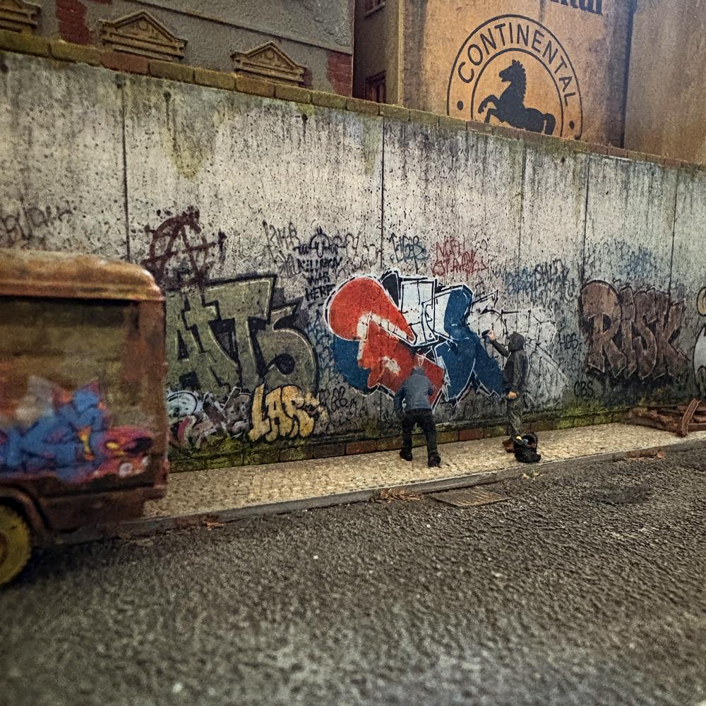 H0-Diorama mit zwei Figuren vor einer gealterten Betonwand mit Graffiti, Tags, Schmutzspuren und verwittertem Gehweg.